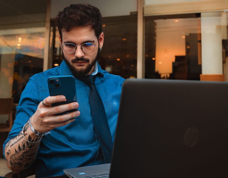 Bearded professional using a smartphone beside a laptop
