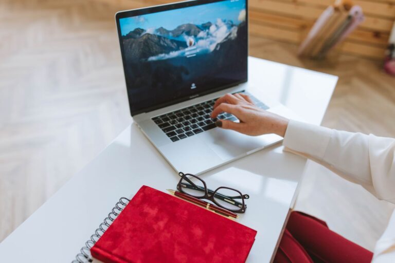 Laptop, red notebook and glasses on a white desk