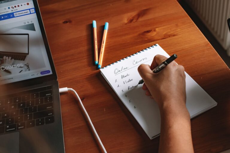 Writing a list on a notepad next to a laptop